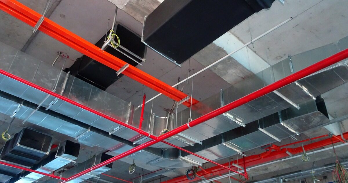 Exposed ceiling services in a building: galvanised air ducts, red sprinkler pipes and cable conduit