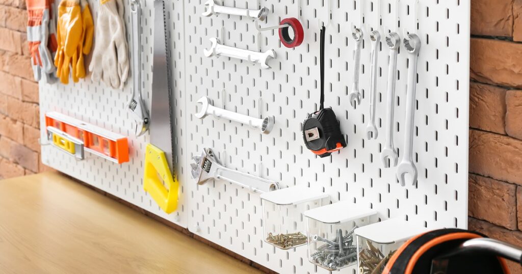 A white pegboard tool wall hung with spanners, a saw, a spirit level and bins of screws